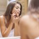 woman popping pimple in front of mirror