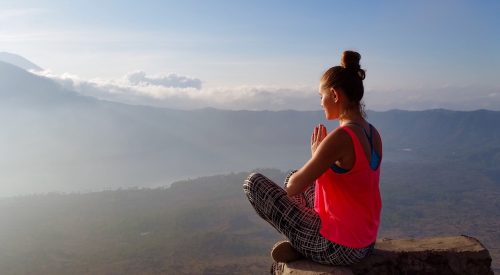 woman meditating at the top of a mountain at sunrise